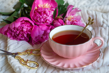 Delicate peony flowers and a cup of aromatic tea on the table.