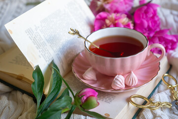 Delicate peony flowers and a cup of aromatic tea on the table.