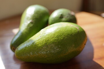 Three ripe green avocados sit on a wooden table, ready for healthy eating and culinary creations