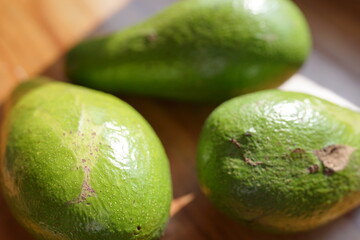 Three fresh avocados on a wooden surface, showcasing their vibrant green skin and healthy goodness