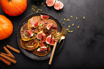 Pumpkin pancakes with honey, pumpkin seeds and figs on a black background. Concept of cozy homemade autumn food. Top view
