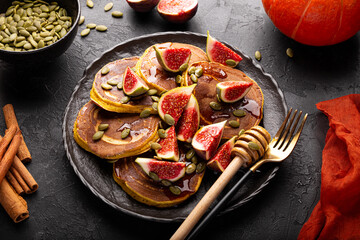Pumpkin pancakes with honey, pumpkin seeds and figs on a black background. Concept of cozy homemade autumn food