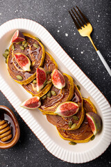 Pumpkin pancakes with honey, pumpkin seeds and figs on a grey background. Concept of cozy homemade autumn food. Top view, vertical photo.