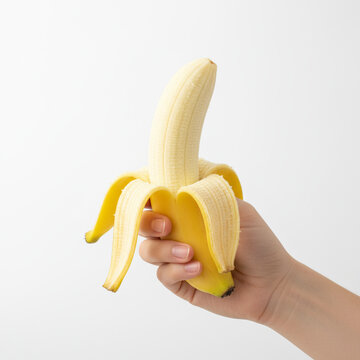 hand holding a perfectly peeled, ripe yellow banana. The lower part of the banana is still in the peel