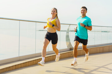 Obraz premium Couple enjoys morning jog along waterfront promenade in activewear
