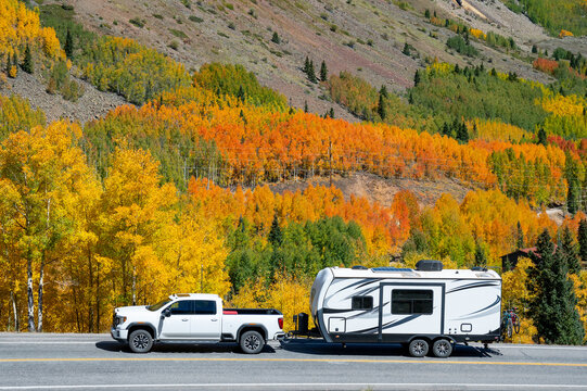 Pickup truck with travel trailer on scenic country road with stunning view of colorful fall foliage on the mountain hill. Autumn landscape in Colorado, USA. Road trip and camping journey