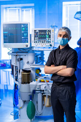 Doctor near monitors in operating room. Medical professional in black uniform and mask standing...