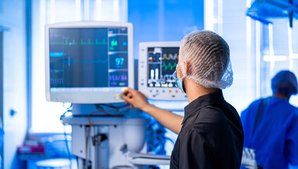 Medical professional adjusting monitoring equipment. Doctor in black uniform and mask adjusting settings on patient monitoring device in the operating room.