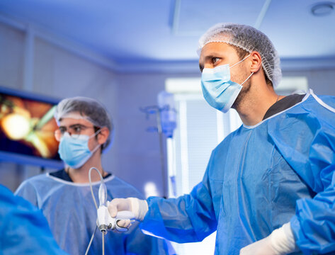 Surgeons performing laparoscopic procedure. Group of doctors in surgical gowns performing laparoscopic procedure in hospital.