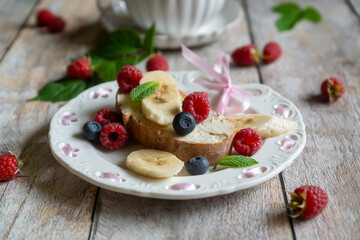 For breakfast, there are toasts with fruits and berries and a cup of aromatic tea on the table.
