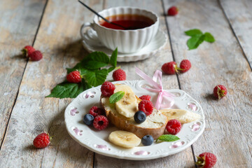 For breakfast, there are toasts with fruits and berries and a cup of aromatic tea on the table.