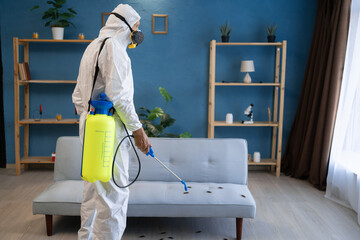Pest control worker exterminating cockroaches at home. Man in white protective workwear spraying...
