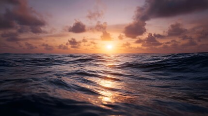 A stunning sunset casts a golden glow over the calm ocean waves and dramatic clouds