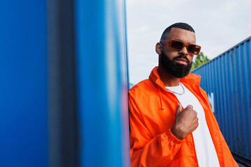 Trendy african american man in sunglasses standing near cargo containers in port 