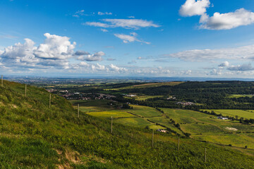Mountain view overlooking valley and meadows with distant city on horizon, partly cloudy sky and expansive natural landscape