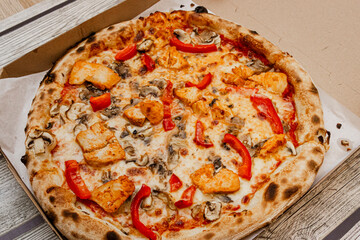 Delicious pizza topped with chicken, mushrooms, and red bell peppers in an open pizza box on a rustic wooden table, perfect for food lovers and casual dining.