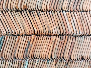 a dense pile of building materials, traditional used clay roof tiles, arranged at an angle and overlapping each other orange-terracotta in color,