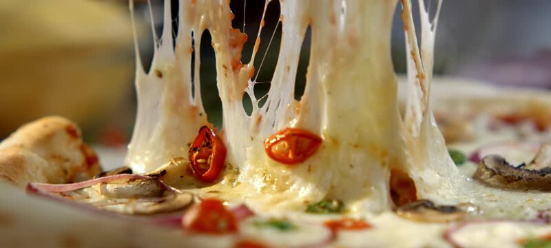 Vertical video of close-up of a person taking a slice of hot vegetarian pizza with mushrooms, red onion, and chili peppers, showcasing the incredible melted mozzarella cheese stretching in slow motion