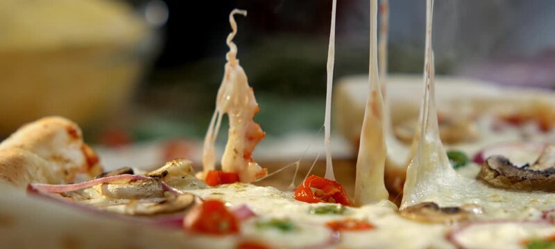 Delicious close-up view of a person taking a slice of freshly baked italian pizza with mushrooms, onions, and tomatoes, showing the cheese stretching in a satisfying and appetizing manner