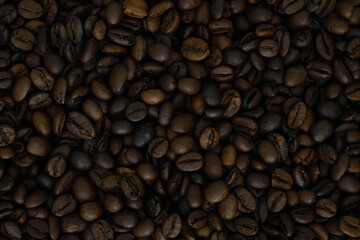 Close-up texture of roasted coffee beans. Dark brown background made of aromatic coffee seeds, top view.