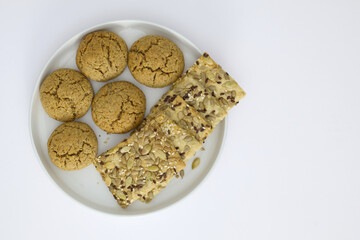 A white plate with oatmeal cookies and seed crackers served next to a cup of black coffee on a white background. Minimalist breakfast or snack concept.