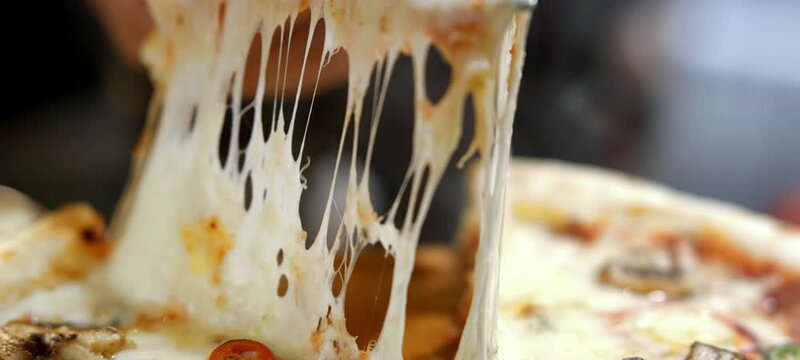 Vertical video of delicious slice of hot pizza with melting mozzarella cheese being lifted up, showing the cheesy pull from the rest of the pie with mushrooms, onions, and spicy chili peppers