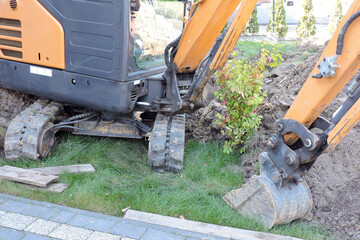 A narrow bucket, a dipper and hydraulic cylinders of a black and yellow mini hydraulic excavator standing in a courtyard next to heap of dirt