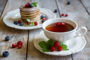 Delicate pancakes with fruits and berries on a wooden table.