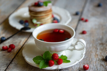 Delicate pancakes with fruits and berries on a wooden table.