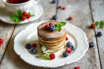 Delicate pancakes with fruits and berries on a wooden table.