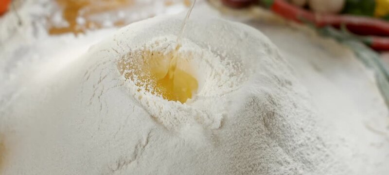 Slow motion shot showing a single egg yolk falling into a mound of white flour, a classic step in preparing dough for fresh pasta, bread, or delicious homemade cakes in a bakery kitchen
