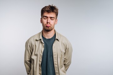 Young man with a sad expression stands against a plain background in casual attire during indoor time