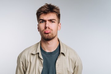 Pouting young man with tousled hair and casual attire against a plain backdrop