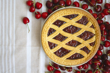 Freshly baked cherry pie surrounded by ripe cherries on a table, copy space