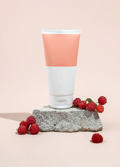 Facial cream unbranded tube mockup on a stone podium and raspberry berries on a beige background