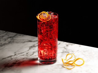 Vibrant red cocktail with orange garnish on a marble surface against a black background.