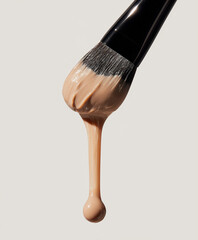 Close-up of a makeup brush with foundation dripping against a neutral background.