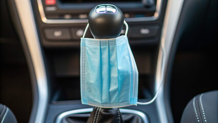 Ride hailing apps simplify urban transportation. A face mask rests on a car gear shift, symbolizing health safety in transportation.