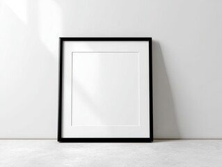 A blank black frame against a white wall, casting shadows on a concrete floor