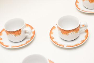 Elegant porcelain tea cups and saucers with intricate orange pattern on white table
