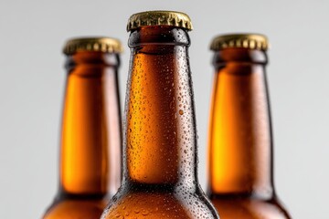 Three brown glass beer bottles with condensation droplets stand elegantly against a white background. Their smooth curves and textures are highlighted, creating a clean and minimal aesthetic.