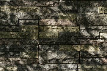 Texture of stacked stone wall tiles with a naturally rough surface. Shadow across the surface, adding a natural aged by weather. For backgrounds, design and 3D rendering materials