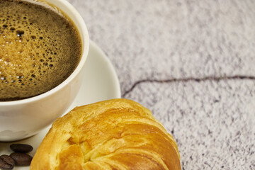 Cup of coffee, close-up, with freshly roasted beans and a croissant to enjoy, copy space and foreground photo.