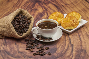 Cup of coffee, close-up, with freshly roasted beans and a croissant to enjoy, copy space and foreground photo.
