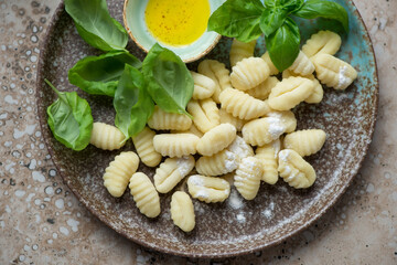 Brown plate with raw italian gnocchi, fresh green basil leaves and olive oil, horizontal shot, middle close-up, elevated view