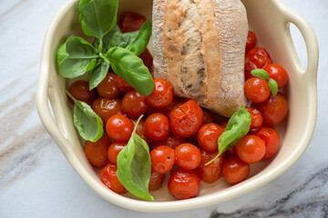 Beige serving tray with roasted cherry tomatoes, green basil and fresh bread, horizontal shot, middle close-up