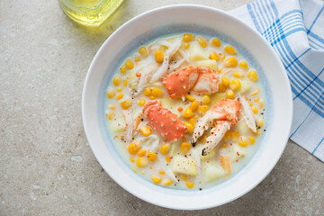 Plate with crab and corn chowder on a beige stone background, horizontal shot, high angle view