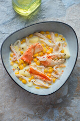 Bowl of corn chowder with crab on a beige and blue stone background, vertical shot, high angle view