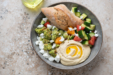 Hummus, falafel and vegetable plate with fresh bread, horizontal shot on a beige granite background, elevated view