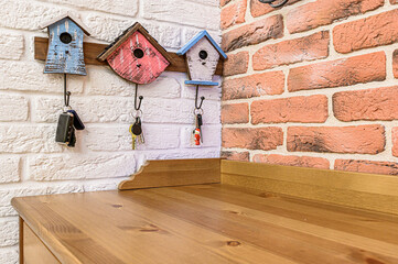 Rustic home interior featuring birdhouse key holders on a white brick wall, with a wooden counter below and brick-patterned wallpaper on the side
